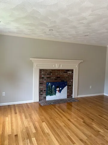 a view of an empty room with wooden floor and a fireplace