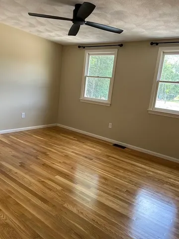 an empty room with wooden floor chandelier fan and windows