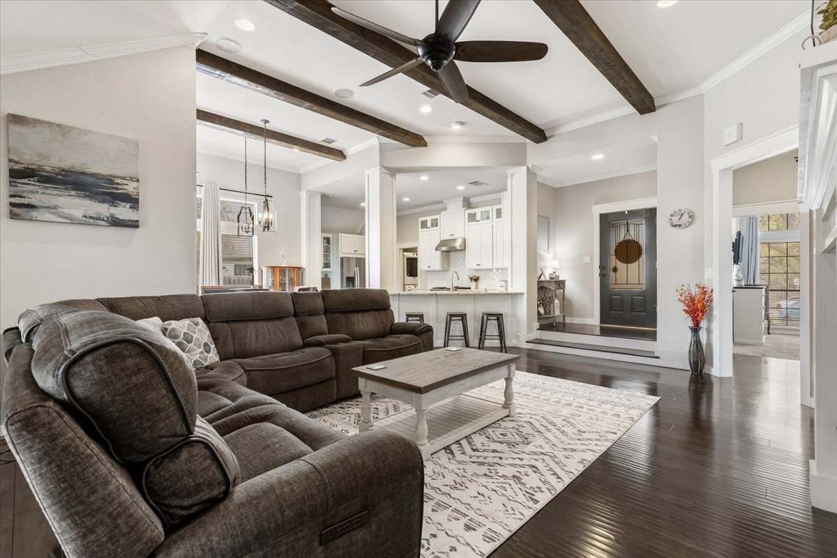701 South Stuart Cove Leander, TX 78641 - Photo 1 of 1 Living room featuring crown molding, a ceiling fan, dark wood-style flooring, beam ceiling, and a chandelier