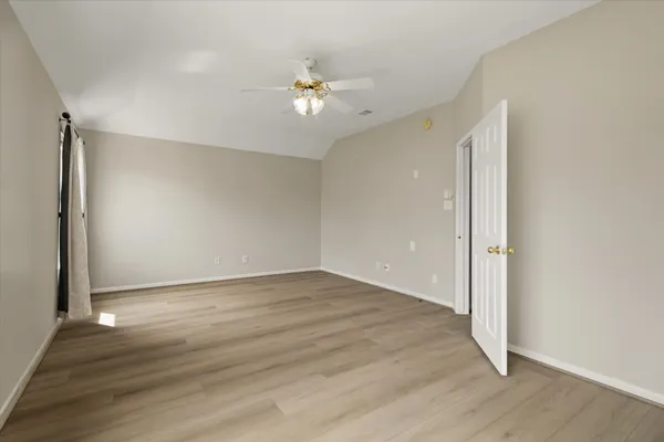 an empty room with wooden floor fan and windows