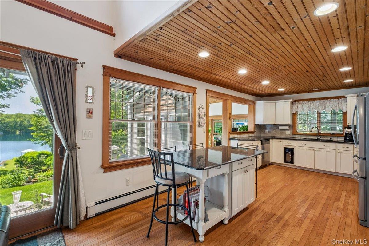 342 Lake Shore Road Putnam Valley, NY 10579 - Photo 11 of 46 Kitchen with water views, stainless steel appliances, baseboard heating, white cabinets, light wood finished floors, and wooden ceiling