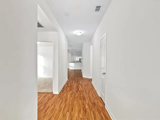 a view of a hallway with wooden floor and a bathroom