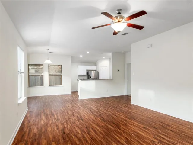 a view of an empty room with wooden floor and a kitchen