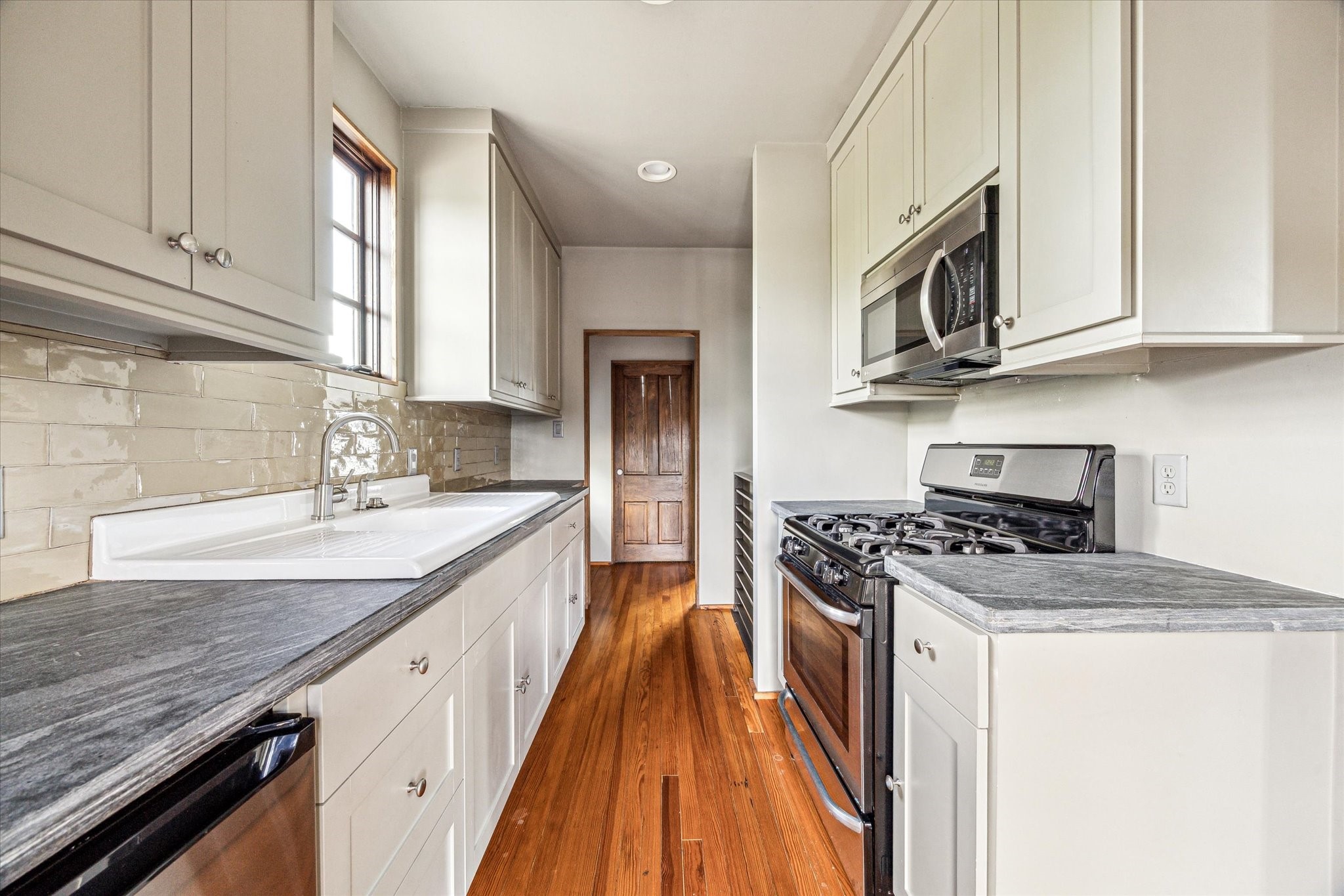 808 Coronado Street Houston, TX 77009 - Photo 25 of 50 Unit 1, galley-style kitchen with white cabinetry, stone counters, and stainless appliances.