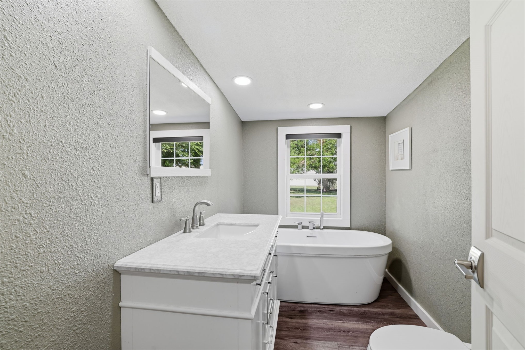 210 Main Caddo, OK 74729 - Photo 11 of 30 Bathroom featuring a white freestanding soaking tub, wood-finish flooring, a white vanity with a light-colored countertop, and a window with exterior views