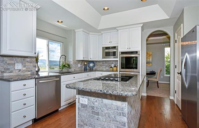 15190 Ridgefield Lane Colorado Springs, CO 80921 - Photo 11 of 31 Kitchen has granite counters, brick tile backsplash, hardwood flooring, stainless appliances including double ovens, and flat top downdraft range on center island...