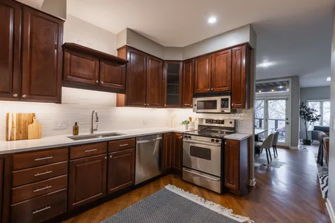 a kitchen with stainless steel appliances granite countertop wooden cabinets a sink a stove a refrigerator and island with wooden floors