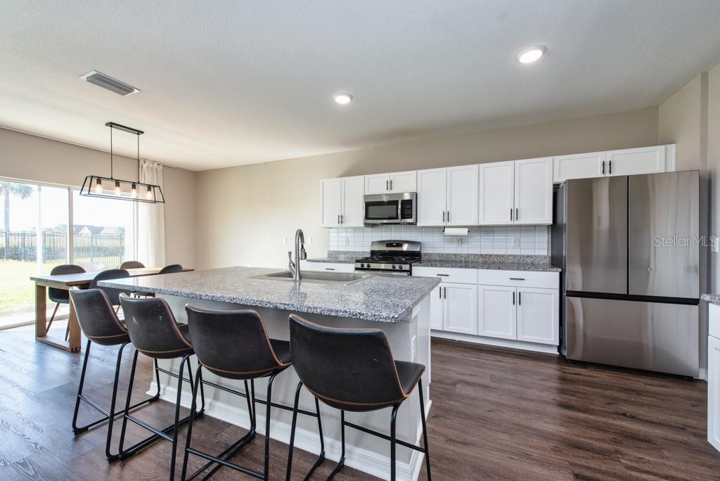 14617 Brumby Ridge Avenue Lithia, FL 33547 - Photo 10 of 46 a kitchen with kitchen island granite countertop wooden floors appliances and white cabinets