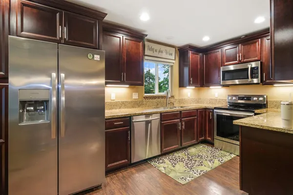 a kitchen with kitchen island granite countertop wooden cabinets a sink a stove a refrigerator and island with wooden floor