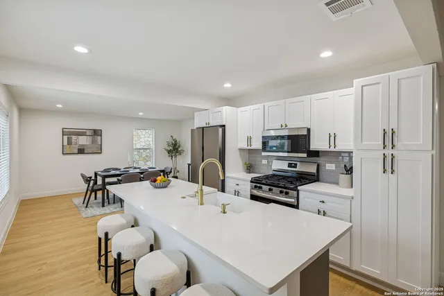 a kitchen with granite countertop a refrigerator a stove a sink a dining table and chairs with wooden floor