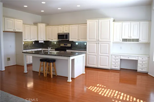 a kitchen with stainless steel appliances granite countertop a stove a sink dishwasher a refrigerator and white cabinets with wooden floor