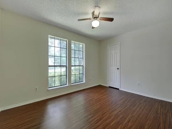 an empty room with wooden floor chandelier fan and windows