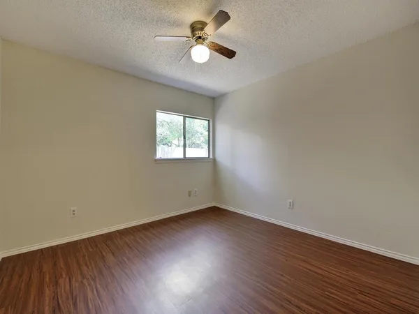 an empty room with wooden floor ceiling fan and windows