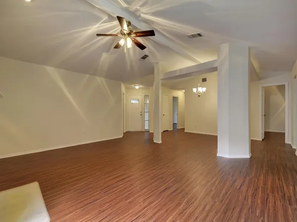 a view of an empty room with wooden floor and a ceiling fan