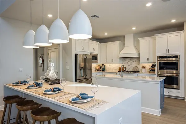 a kitchen with stainless steel appliances kitchen island granite countertop a sink a stove a refrigerator and a dining table with white cabinets