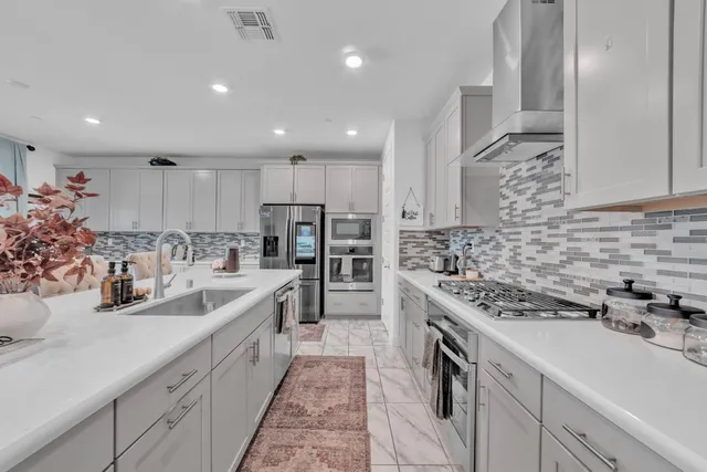 a large white kitchen with stainless steel appliances granite countertop a sink a stove and a refrigerator