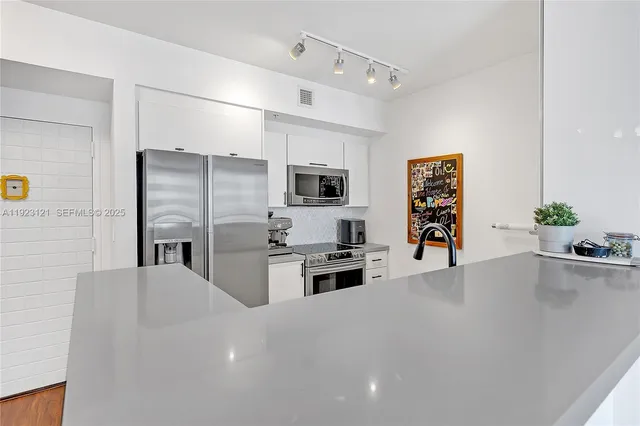 a living room with stainless steel appliances a kitchen island hardwood floor and a sink