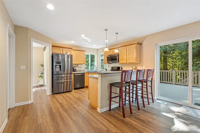 a kitchen with stainless steel appliances granite countertop a refrigerator a stove top oven and a dining table with wooden floor