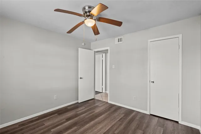 an empty room with wooden floor ceiling fan and windows