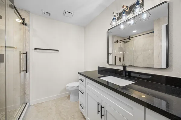a bathroom with a granite countertop sink a toilet a mirror and shower