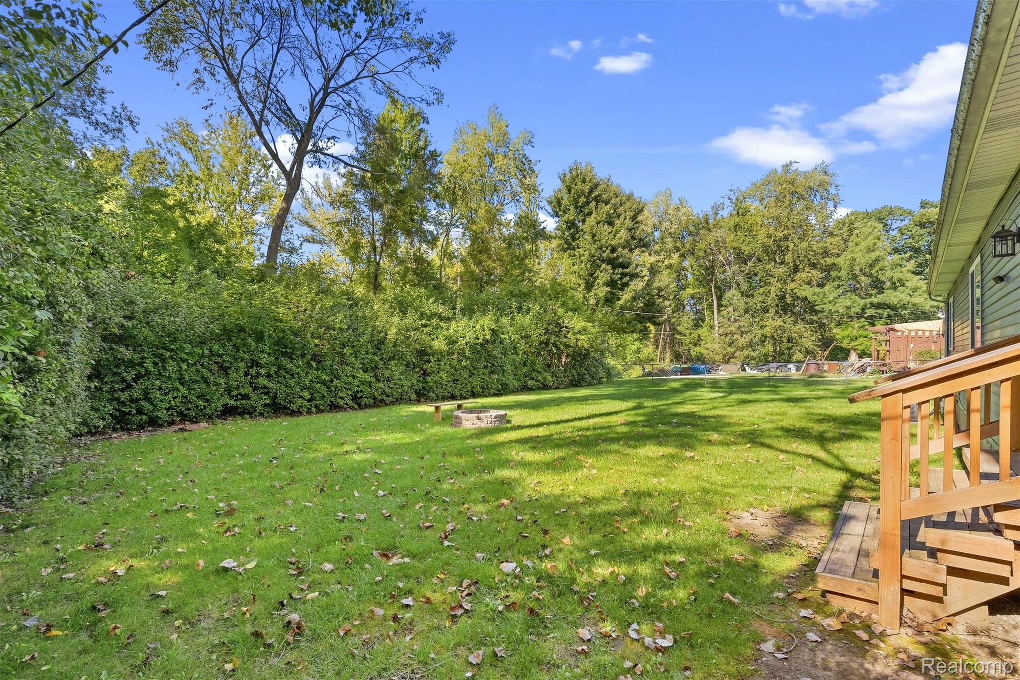 1750 Henbert Road West Bloomfield, MI 48324 - Photo 28 of 32 Expansive grassy yard bordered by mature trees and shrubs, featuring a built-in fire pit