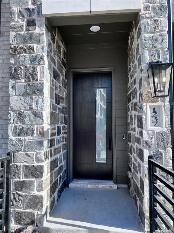1237 Doris May Drive Allen, TX 75013 - Photo 3 of 19 Modern entry featuring a dark wood-finish door with vertical glass insert, stone veneer facade, and contemporary exterior lighting