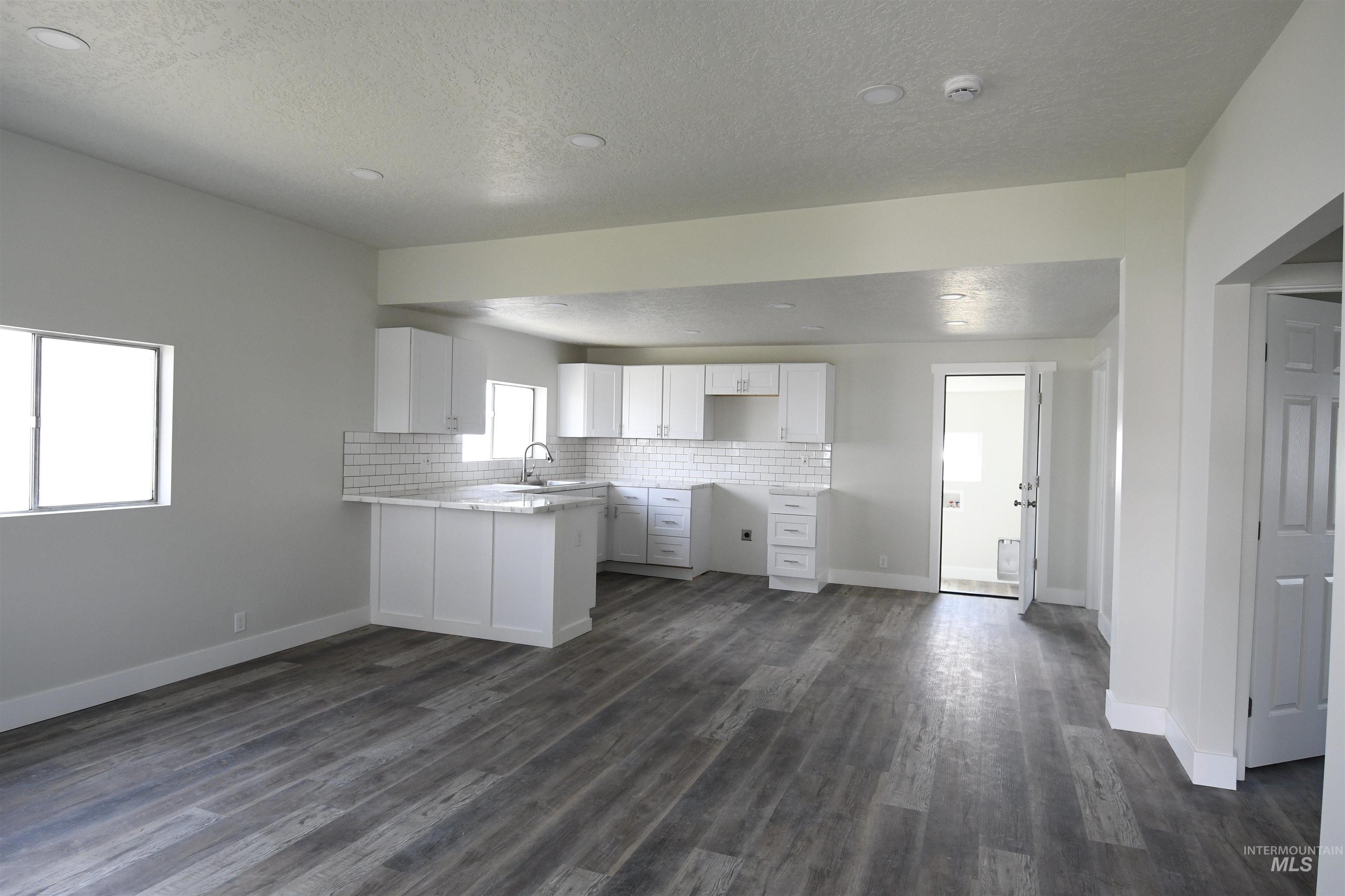 238 West Main Street St. Anthony, ID 83445 - Photo 6 of 9 Kitchen featuring a peninsula, a textured ceiling, tasteful backsplash, white cabinets, and dark wood-type flooring