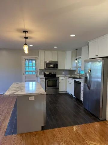 a kitchen with granite countertop a stove top oven a sink dishwasher a refrigerator and a dining table with wooden floor