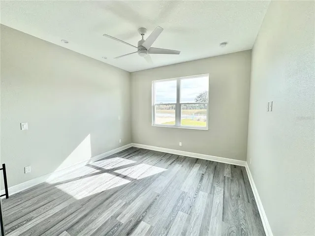 an empty room with wooden floor fan and windows