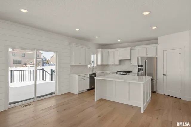 a kitchen with stainless steel appliances a refrigerator a sink a stove and white cabinets with wooden floor