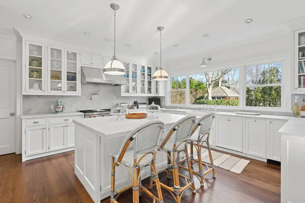a kitchen with kitchen island granite countertop a stove a sink and white cabinets with wooden floors