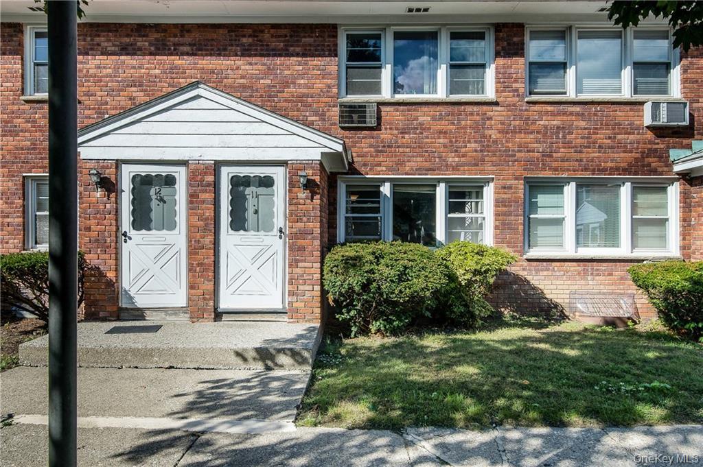 Doorway to property with a wall mounted AC, a yard, and brick siding