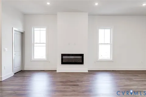 an empty room with wooden floor a kitchen view and windows