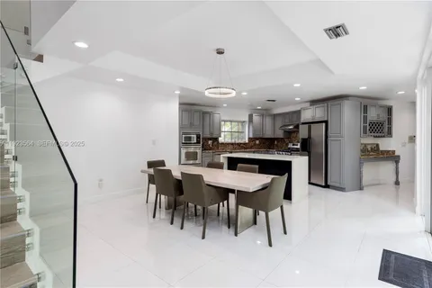 a kitchen with stainless steel appliances kitchen island granite countertop a refrigerator a stove a sink a dining table and chairs with wooden floor