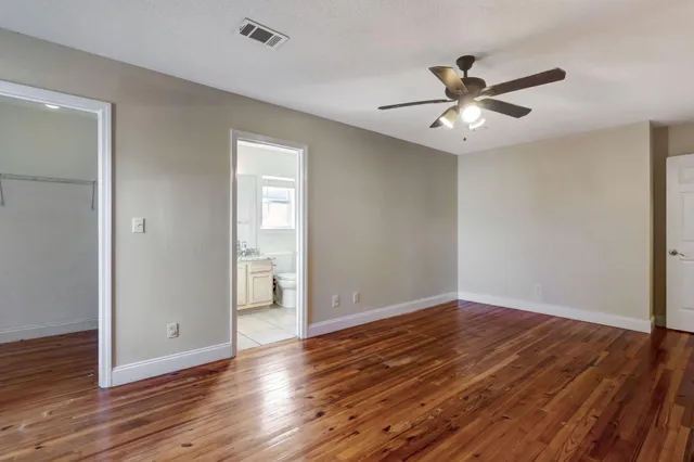 a view of an empty room with wooden floor and a ceiling fan