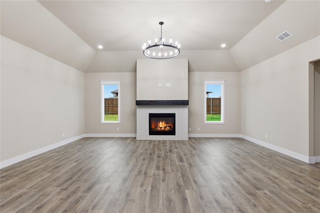 702 Anne Road Van Alstyne, TX 75495 - Photo 8 of 27 Spacious room featuring vaulted ceilings, a central fireplace with a white tile surround and dark wood mantel, recessed lighting, wood-finish flooring, and two windows