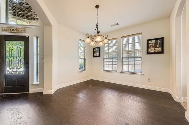 an empty room with wooden floor chandelier and windows