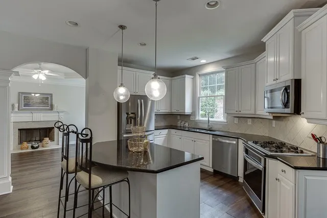 a kitchen with granite countertop a refrigerator a stove a sink and white cabinets with wooden floor