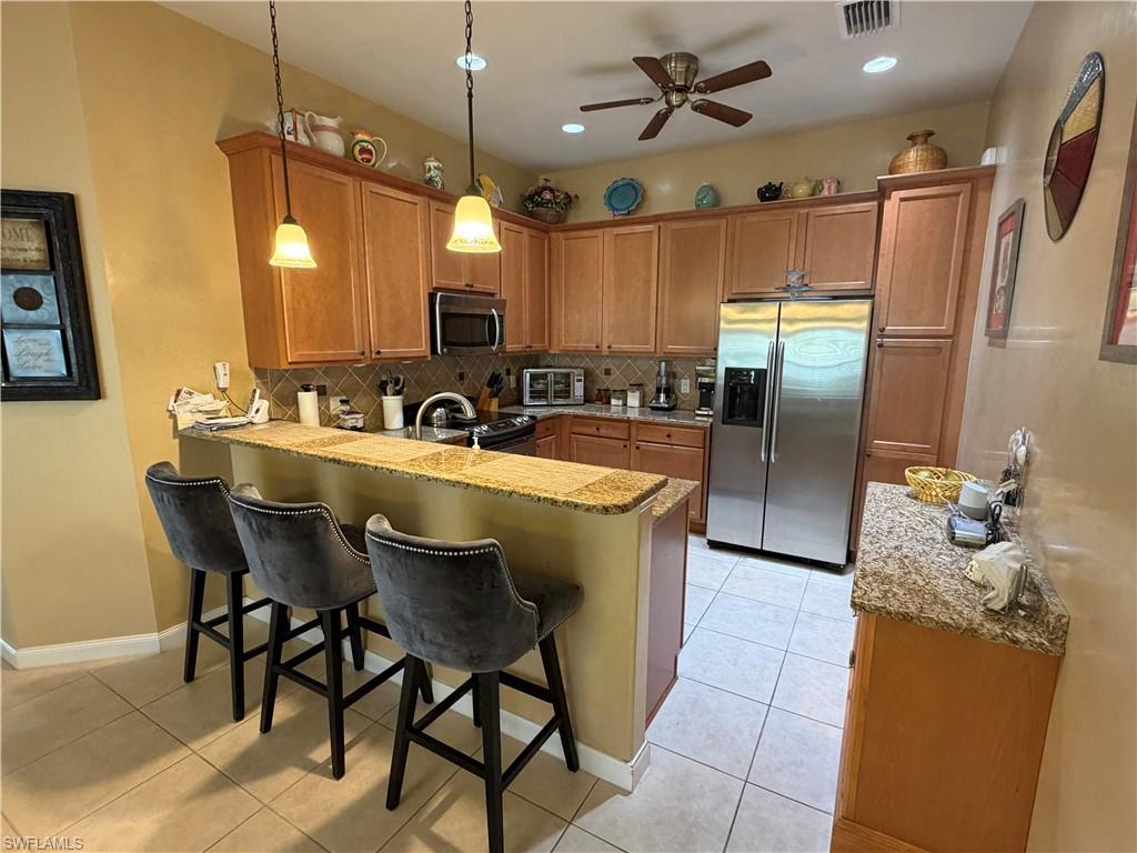 7264 Salerno Court Naples, FL 34114 - Photo 14 of 45 Kitchen with a peninsula, stainless steel appliances, a breakfast bar, decorative light fixtures, and brown cabinetry