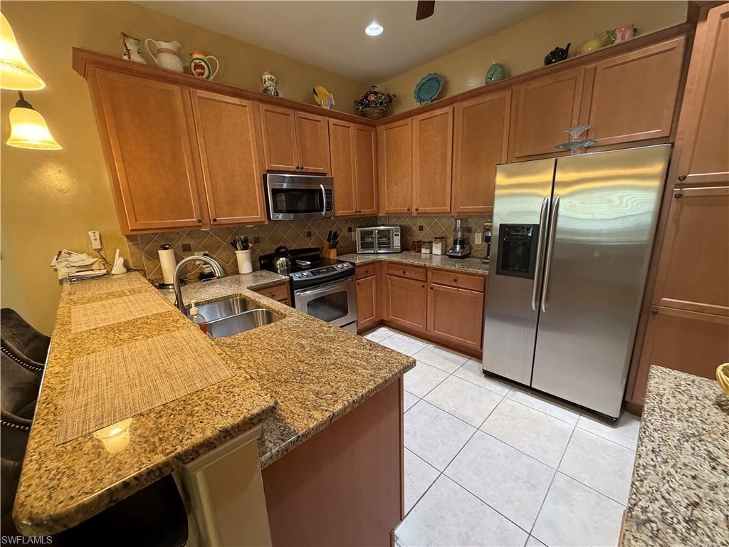 7264 Salerno Court Naples, FL 34114 - Photo 15 of 45 Kitchen with brown cabinetry, stainless steel appliances, light stone counters, tasteful backsplash, and pendant lighting
