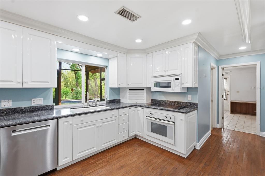 1840 Salem Court Dunedin, FL 34698 - Photo 20 of 64 a kitchen with stainless steel appliances granite countertop white cabinets a sink a window and wooden floors