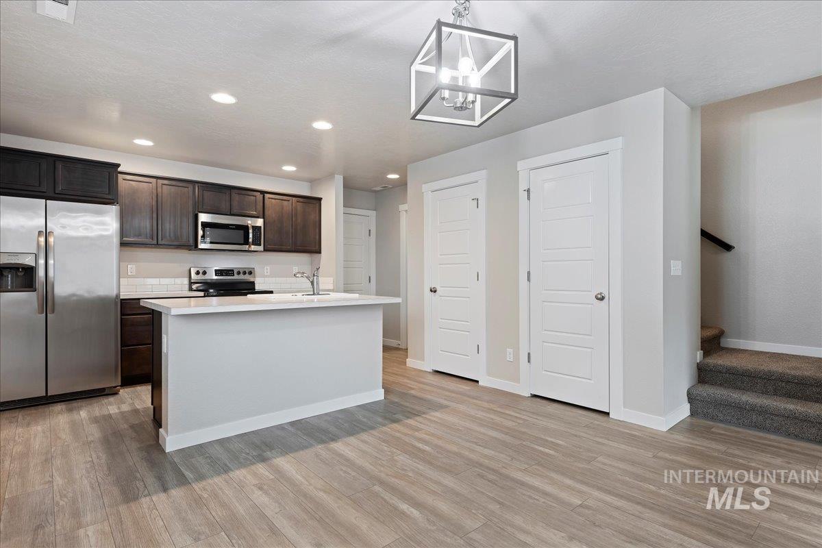 2500 East Blue Tick Street Meridian, ID 83642 - Photo 7 of 24 Kitchen with stainless steel appliances, dark wood finish cabinetry, an island with sink, pendant lighting, and light wood finished floors