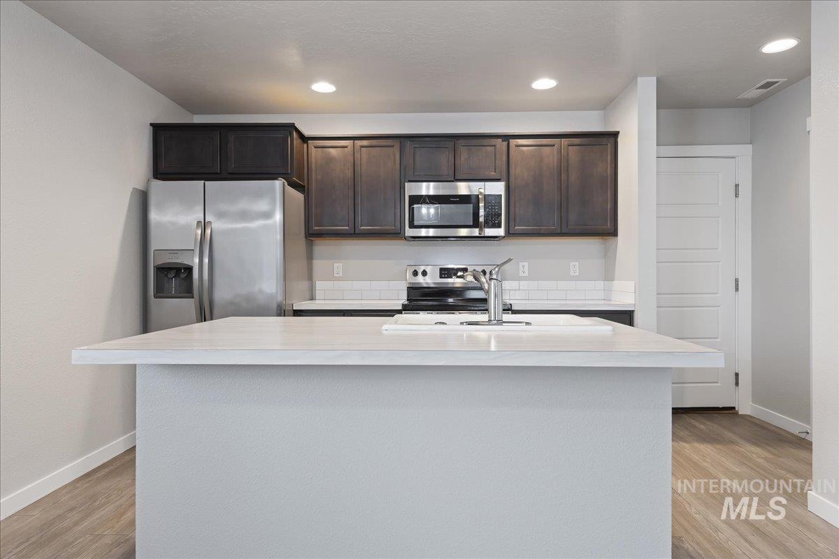 2500 East Blue Tick Street Meridian, ID 83642 - Photo 8 of 24 Kitchen with stainless steel appliances, light countertops, dark wood finish cabinetry, a kitchen island with sink, and recessed lighting