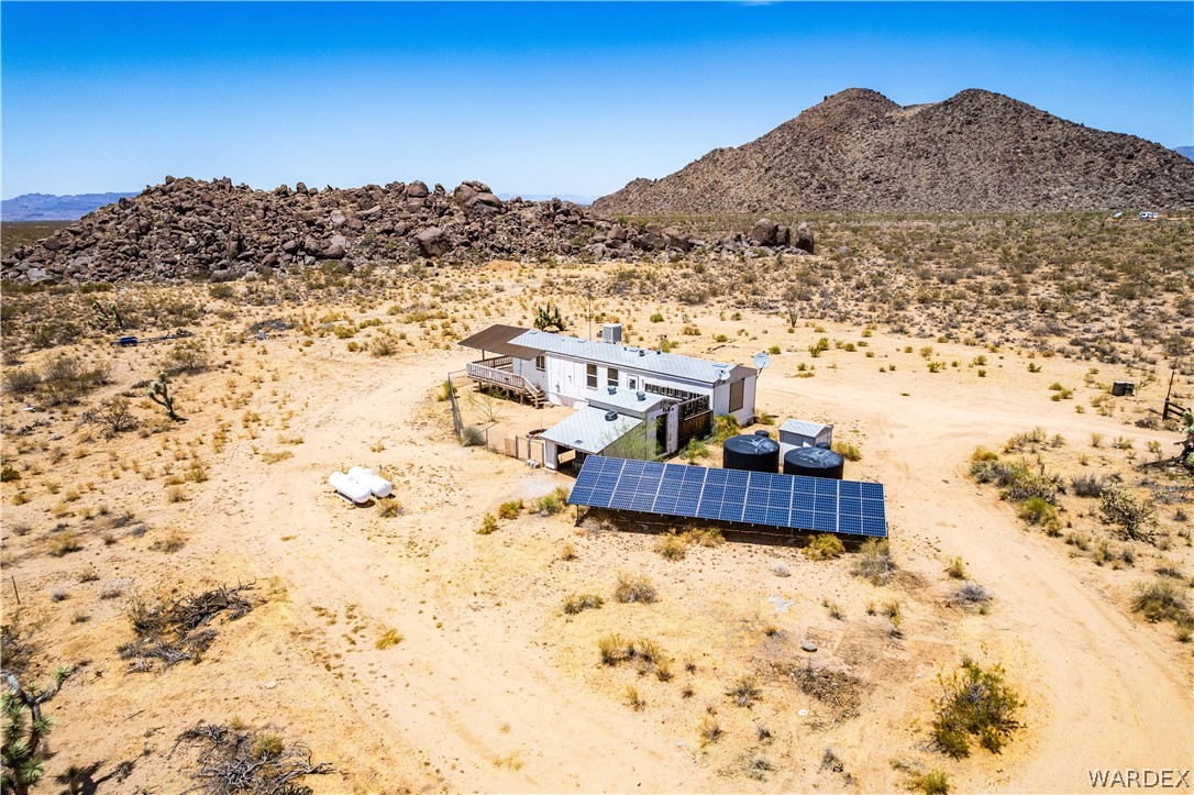 16435 South Wyatt Earp Road Yucca, AZ 86438 - Photo 41 of 57 Desert landscape featuring a single-story residence with an elevated deck, solar panel array, and two large storage tanks