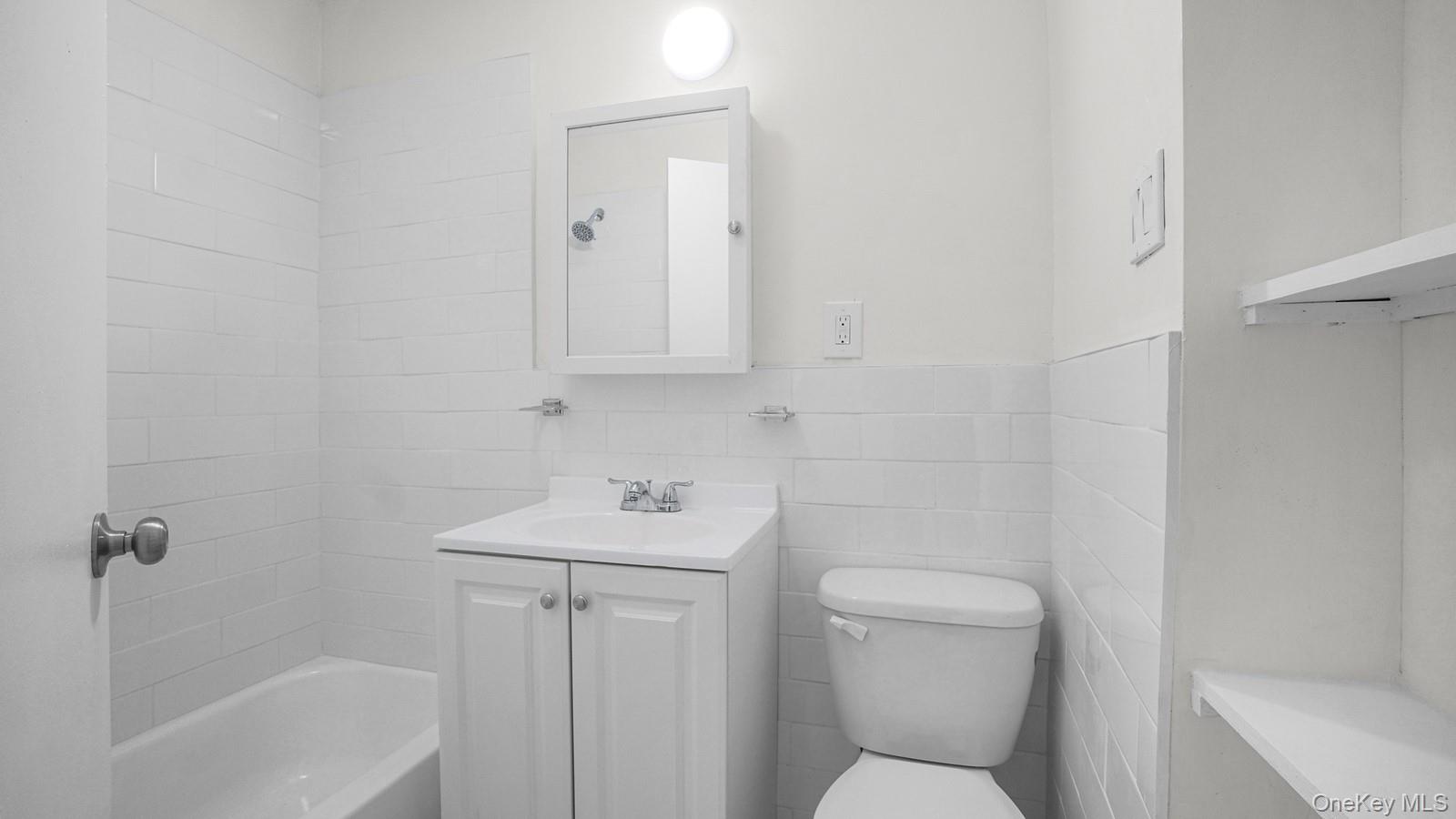 681 Rhinelander Avenue Bronx, NY 10462 - Photo 16 of 30 Full bath featuring tile walls, vanity, bathing tub / shower combination, and wainscoting