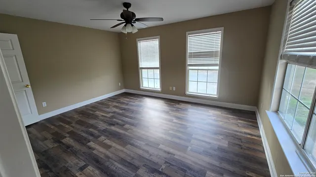 a view of a room with wooden floor a ceiling fan and windows