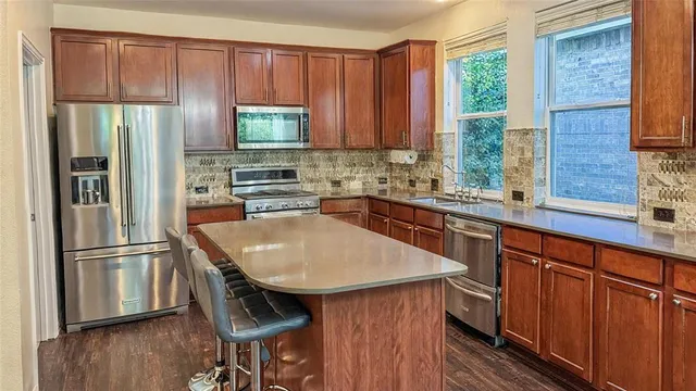 a kitchen with stainless steel appliances a sink a microwave a refrigerator and wooden cabinets