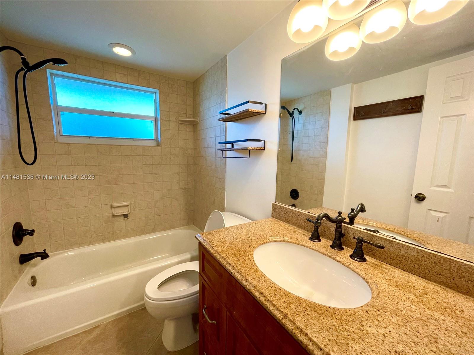 5100 Southwest 90th Avenue, Unit 303 Cooper City, FL 33328 - Photo 23 of 36 a bathroom with a granite countertop sink a toilet a mirror a bathtub and shower