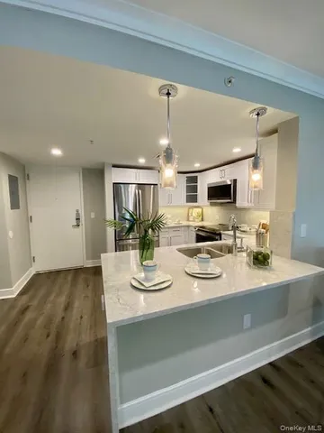 a dining hall with stainless steel appliances kitchen island granite countertop a sink dishwasher and white cabinets with wooden floor