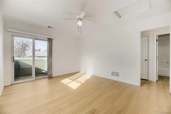 a view of an empty room with wooden floor and a ceiling fan